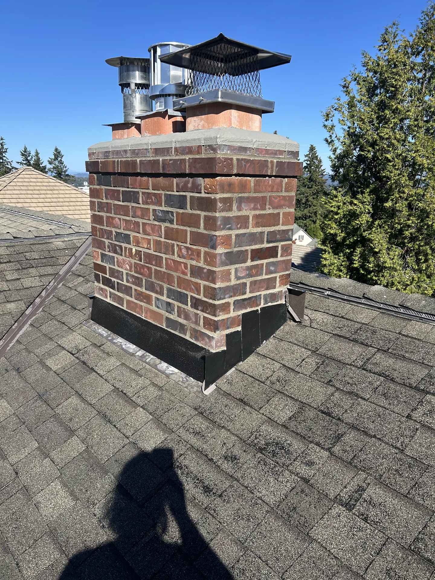 Stainless venting and factory caps on a dark brick chimney installed by First Rate Chimney