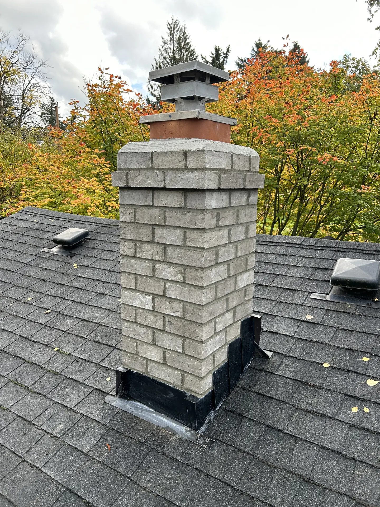 A Harbor Mist gray brick chimney crown rebuilt by First Rate Chimney against fall foliage