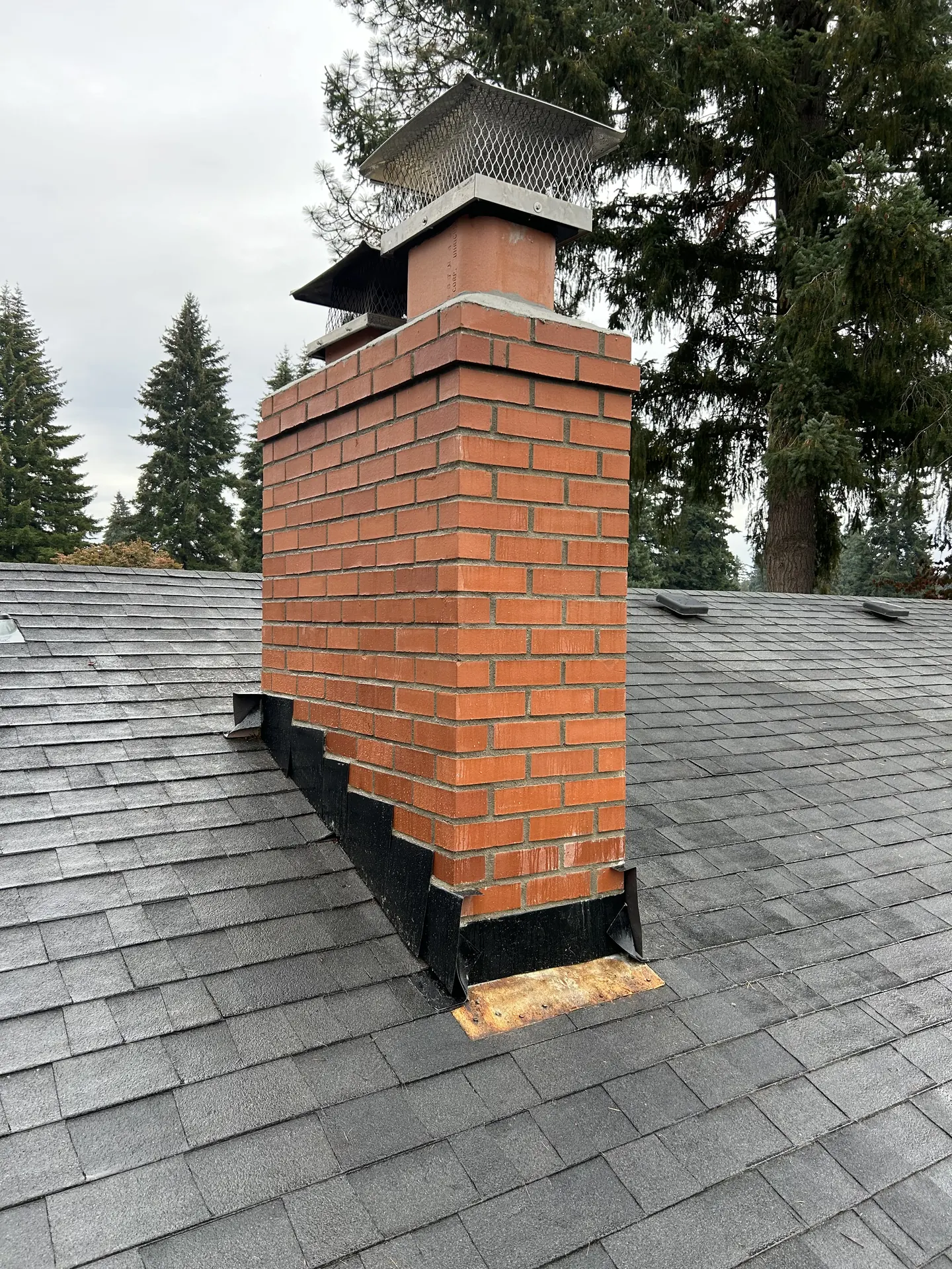 A tall orange brick chimney rebuilt by First Rate Chimney, framed by evergreens near Sandy, Oregon